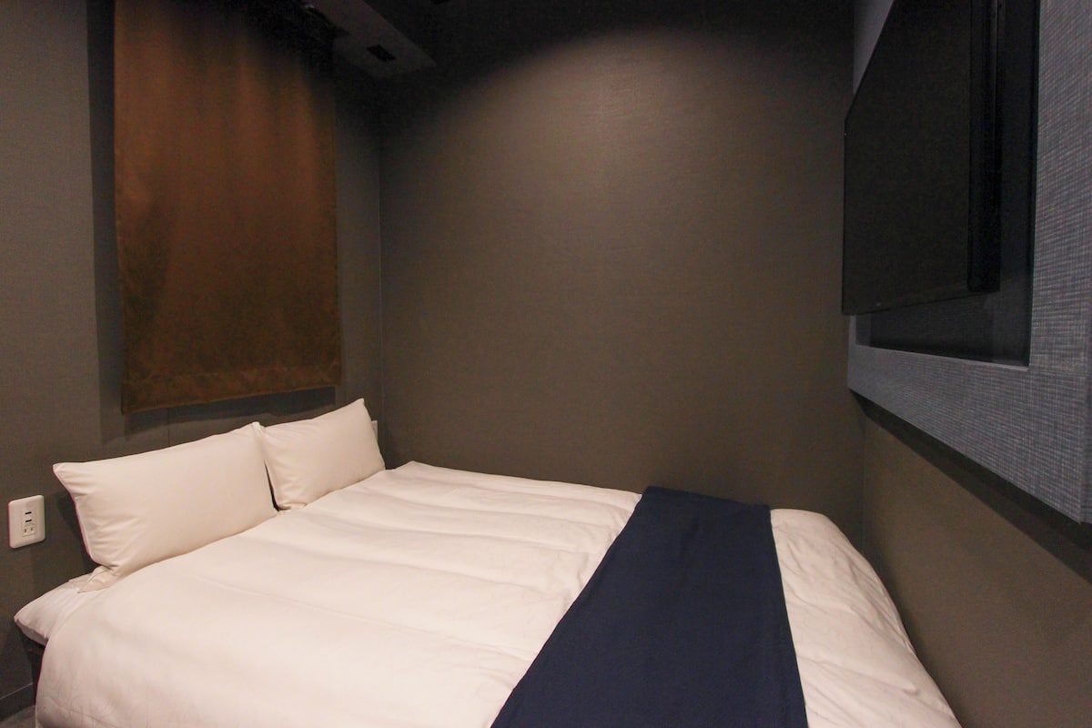 A hotel room with a bed, a wall-mounted TV, and a power outlet.