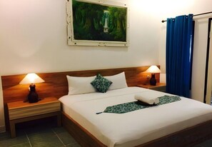 A neatly made bed with white linens, two bedside lamps, a green patterned throw, and a painting of a forest scene above the bed. - Gili White Bamboo by Secoms (Gili Trawangan)