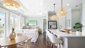 A modern kitchen with a central island, pendant lights, and a dining area with a white table and chairs.