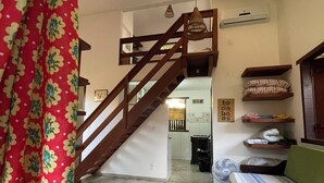 A room with a bed, a fan, a staircase, and a small kitchen area.