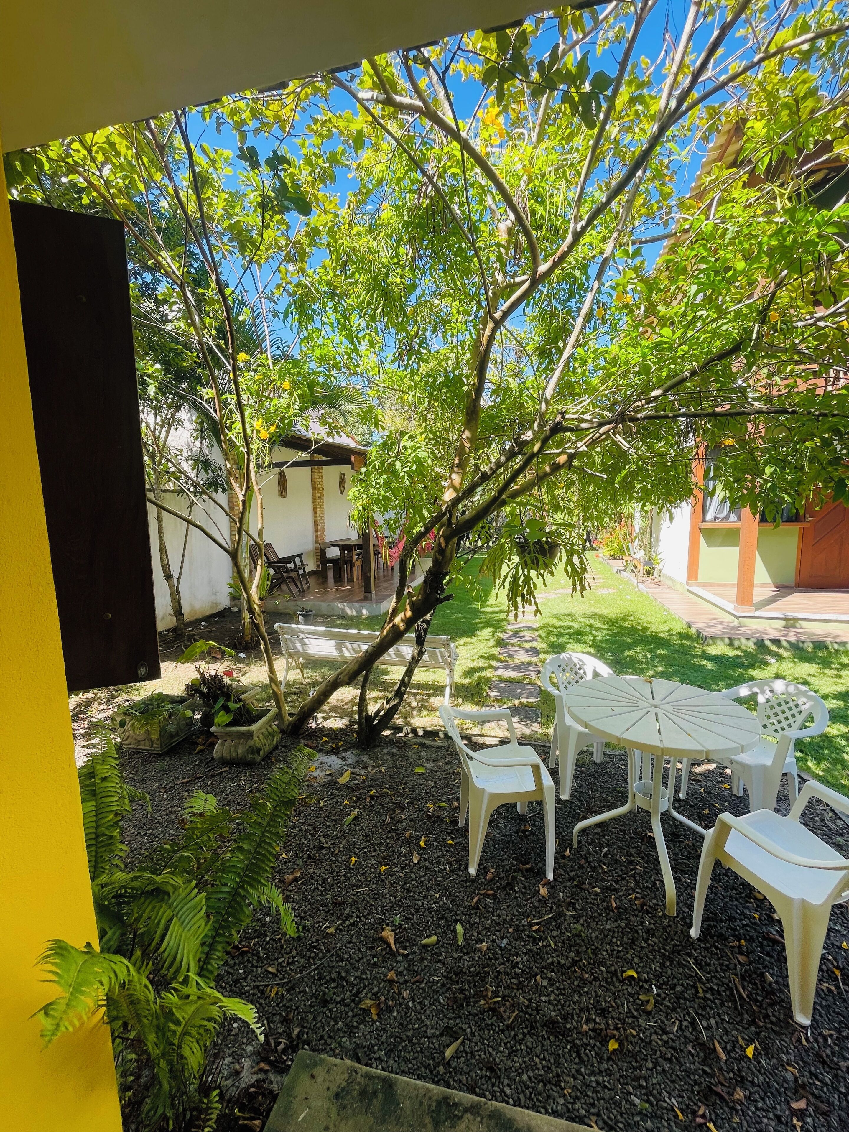 A patio area with a table and chairs, surrounded by greenery and a clear blue sky.