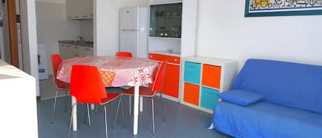 A compact living space with a dining table, chairs, a sofa, a kitchenette, and a colorful cabinet.