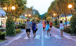 A paved pedestrian street lined with trees and street lamps, with people walking. - Apartment in Porto Santa Margherita (Caorle)