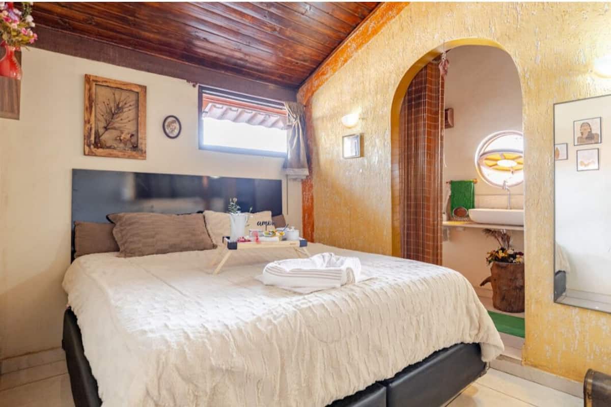 Un dormitorio con cama, mesita de noche, espejo y ventana.