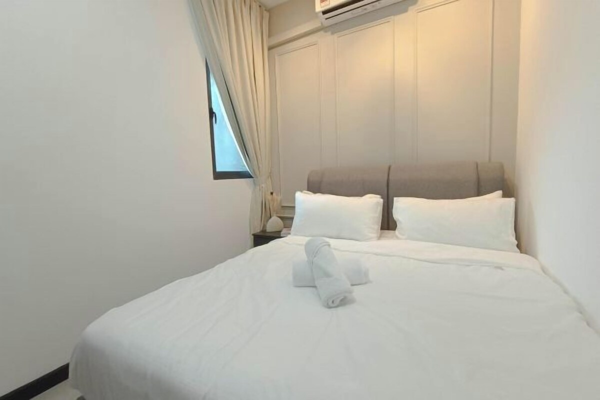 A hotel room with a neatly made bed, a window with curtains, and an air conditioning unit on the wall.