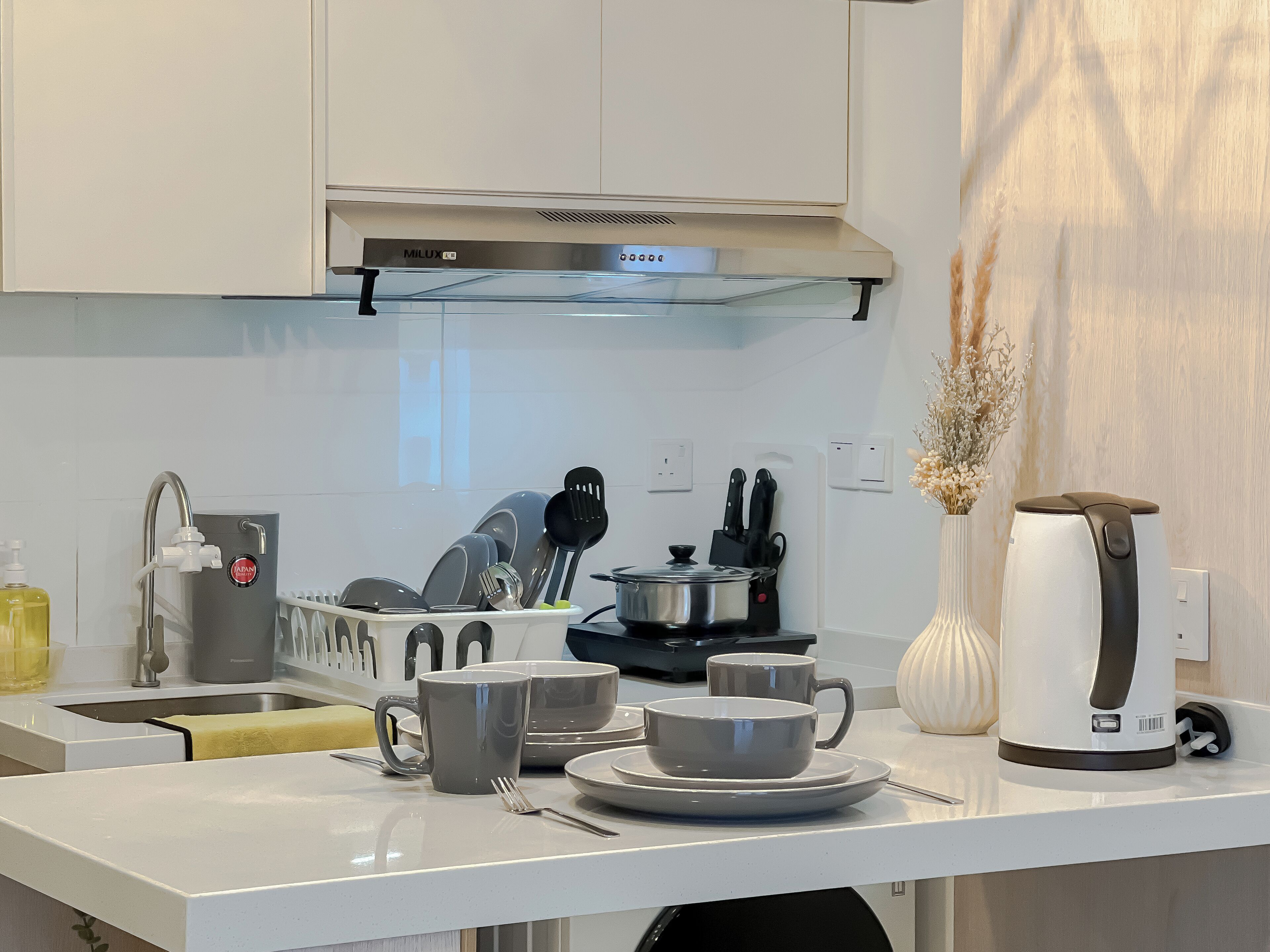 Una cocina moderna con armarios blancos, una campana extractora de acero inoxidable, un escurreplatos y una cafetera.
