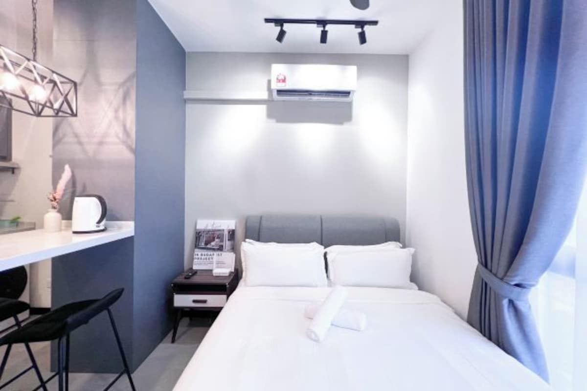 A modern hotel room with a bed, bedside table, and a small desk with a chair.
