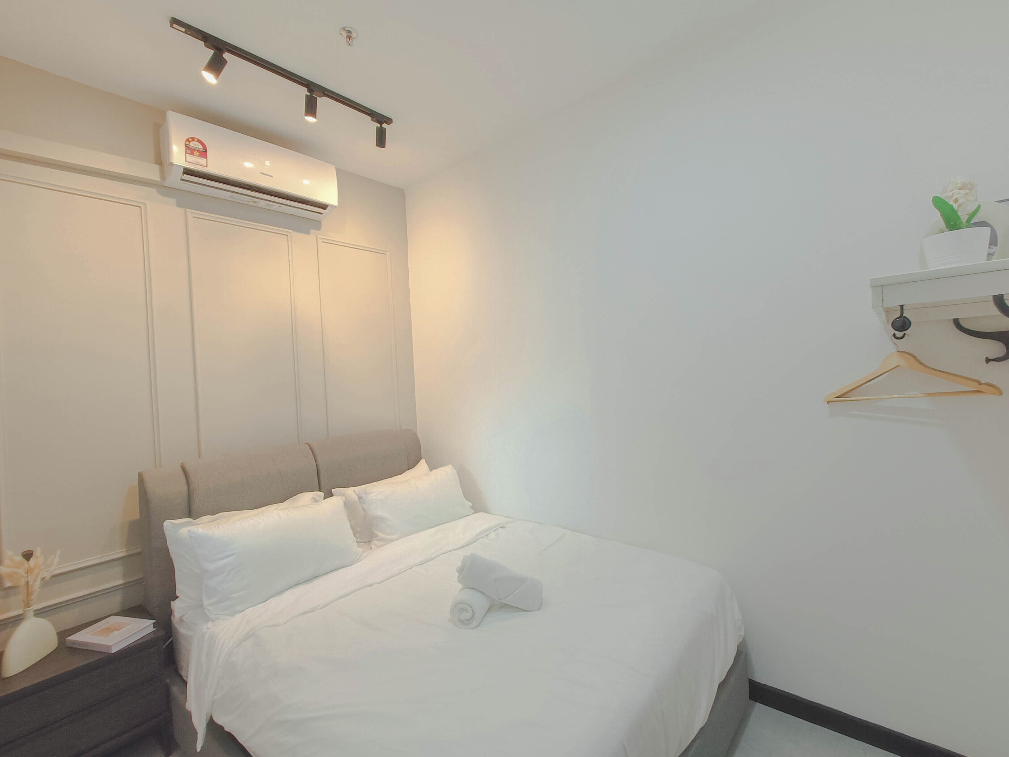 A neatly made bed with white linens, a bedside table with a lamp, and a wall-mounted air conditioner.