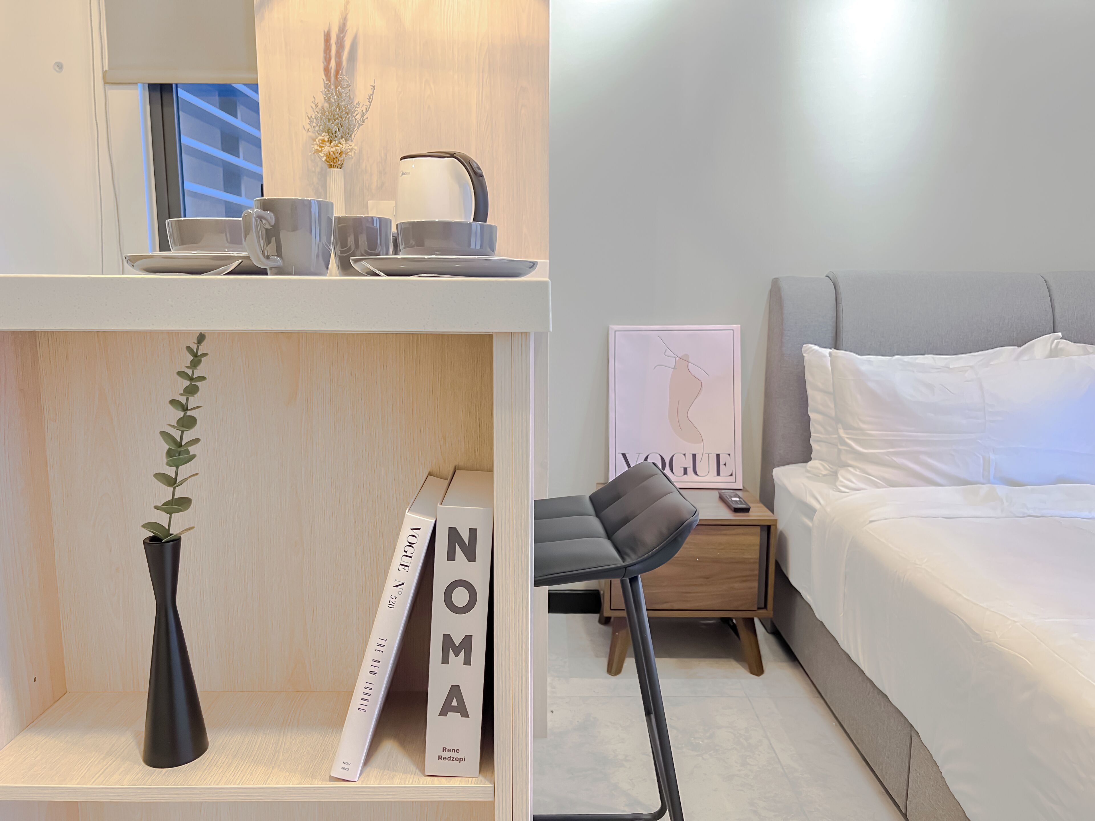 A modern bedroom with a bed, a nightstand, a chair, and a shelf with books and a vase.