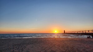 A beach with a pier extending into the water, a sunset in the background, and footprints in the sand.