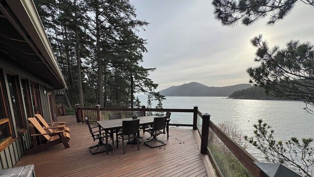 En träveranda med ett bord och stolar, med utsikt över en sjö och berg i fjärran.