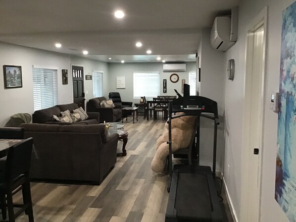 A modern living room with a treadmill, a dining area, and a kitchen in the background.