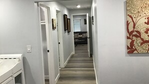 A narrow hallway with a wooden floor, white walls, and a door leading to a living room. - Spacious 4-bedroom house with AC, fitness equipment in wonderful Lakeside (Lakeside)