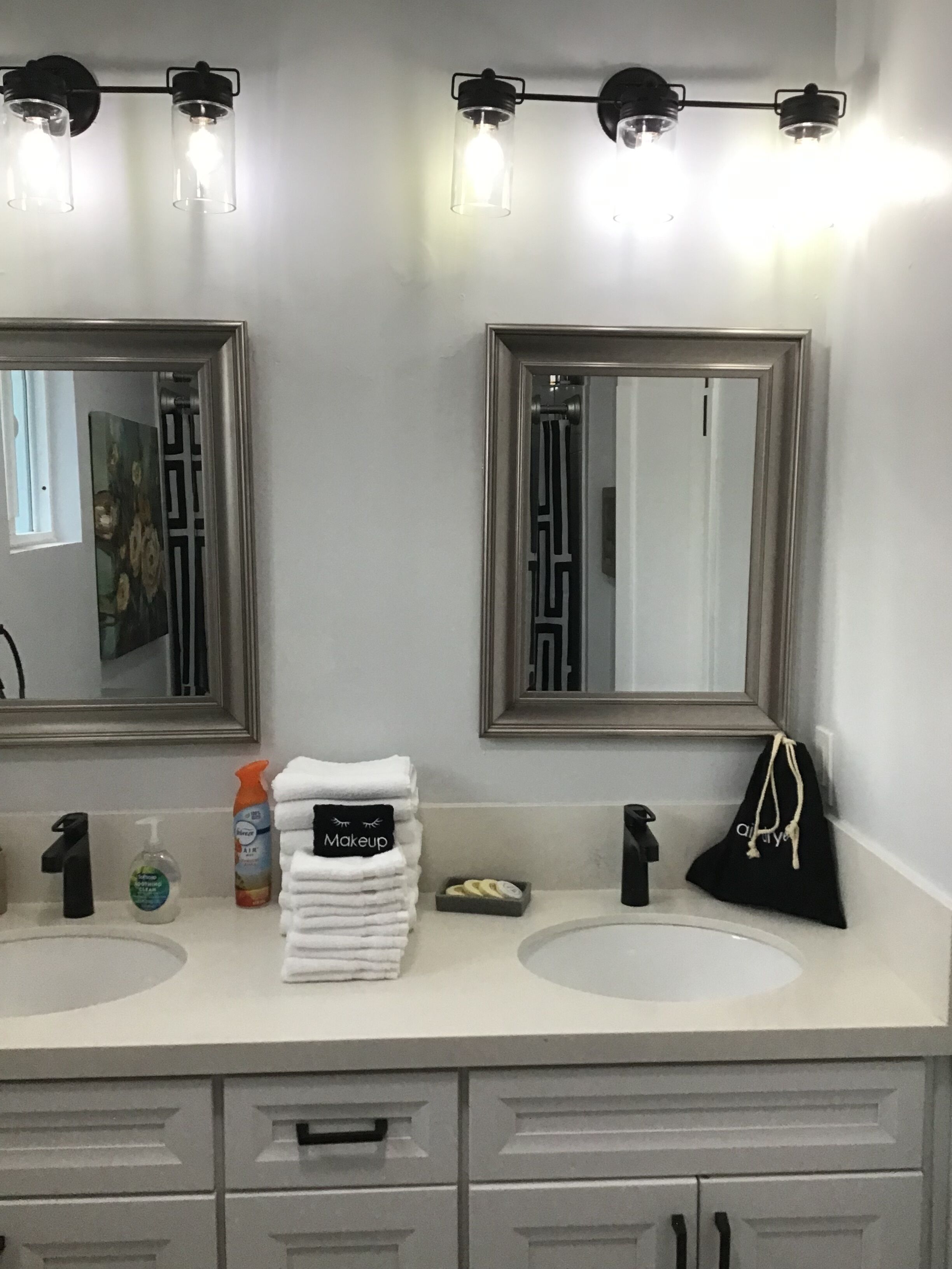 Une salle de bain avec deux lavabos, un miroir et un porte-serviettes. On y trouve des articles de toilette et une trousse de maquillage posés sur le comptoir.