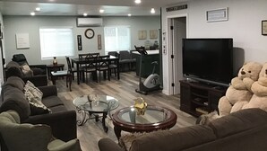 A living room with a sofa, coffee table, TV, and a large teddy bear. - Spacious 4-bedroom house with AC, fitness equipment in wonderful Lakeside (Lakeside)