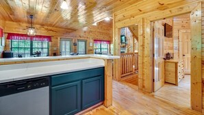 A wooden cabin interior with a kitchen area, wooden walls, and a dining area. - Family Cabin with Hot Tub, Theater, Game Room, Wifi, & Sauna (Sevierville)