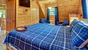 A wooden cabin room with a bed, two chairs, a small table with a tray, and a window with curtains. - Smoky Mountain Views • Sleeps 17 • Theater Rm, Sauna, Arcade, Pavilion & Hot Tub (Sevierville)