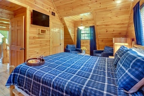 A wooden cabin bedroom with a bed, two chairs, a small table with a tray, and a window with curtains. - Top-Ranked Cabin! Great Amenities! Perfect Location! Secluded Hideaway. Ez Roads (Sevierville)
