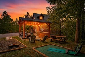 Eine Holzhütte mit überdachter Terrasse, Sitzgelegenheit im Freien und Blick auf den Sonnenuntergang.