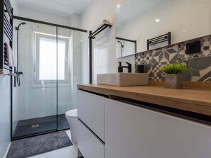 A modern bathroom with a glass shower enclosure, a white toilet, and a wooden vanity with a sink and a potted plant.