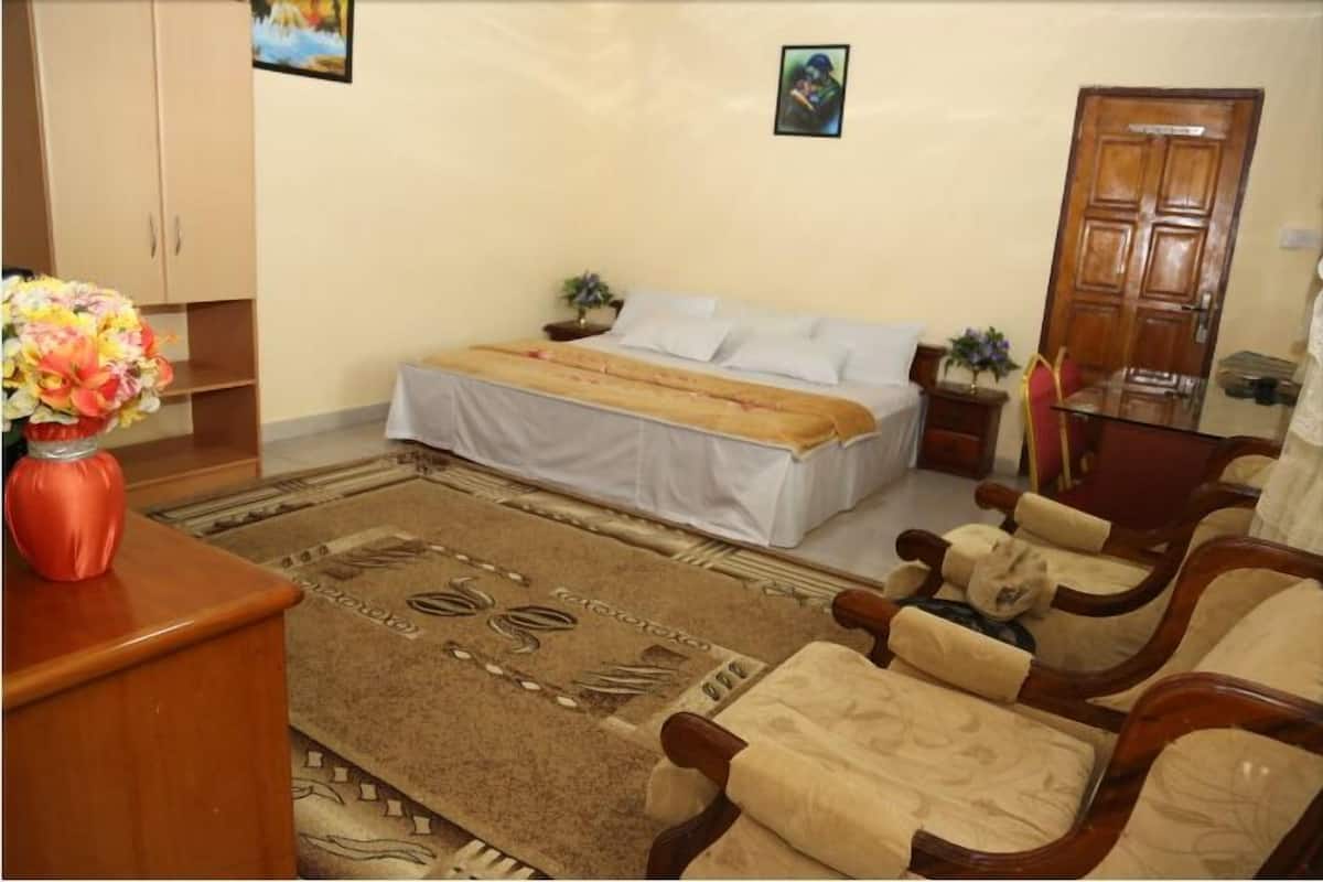Ein Schlafzimmer mit einem Bett, Nachttischen, einem Holzschrank, einem Schreibtisch mit einer Vase und einem gemusterten Teppich.