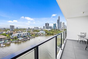 Ein Balkon mit Blick auf eine Stadt, darunter ein Fluss, moderne Gebäude und ein Essbereich.
