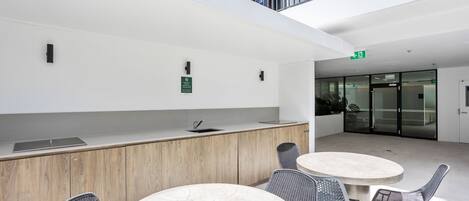 Ein moderner Innenraum mit einer Rezeption, einer Sitzecke mit runden Tischen und Stühlen sowie einer Glastür zu einem weiteren Raum.