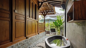 A stone pathway leading to a large bathtub, wooden walls, and a covered seating area with a view of greenery.