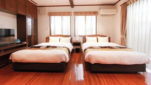 A hotel room with two beds, wooden flooring, a TV, and a desk with a computer.