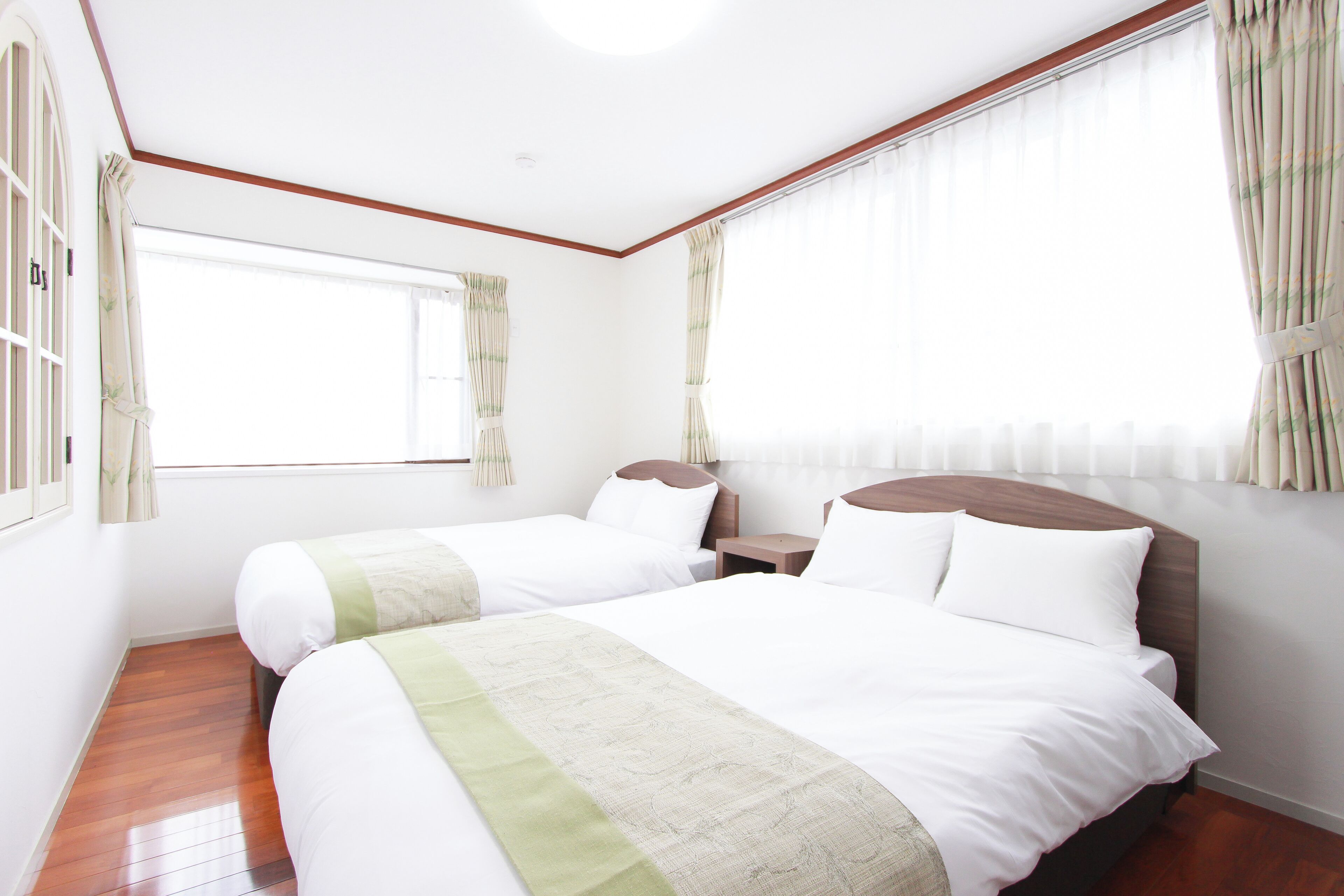 Habitación de hotel con dos camas, piso de madera, un ventanal grande con cortinas y cabecero de madera.
