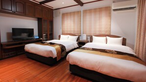 A hotel room with two beds, wooden flooring, a TV, and an air conditioning unit.