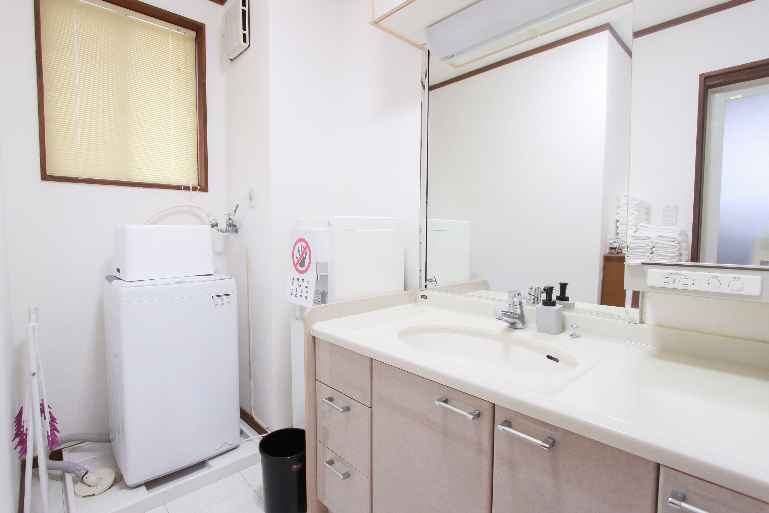 A bathroom with a white sink, mirror, and a small white heater. There is a trash bin and a towel rack.