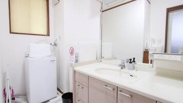 A bathroom with a white sink, mirror, and a small white heater. There is a trash bin and a towel rack.