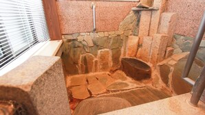 A stone-walled bathroom with a bathtub, a shower area, and a window with blinds.