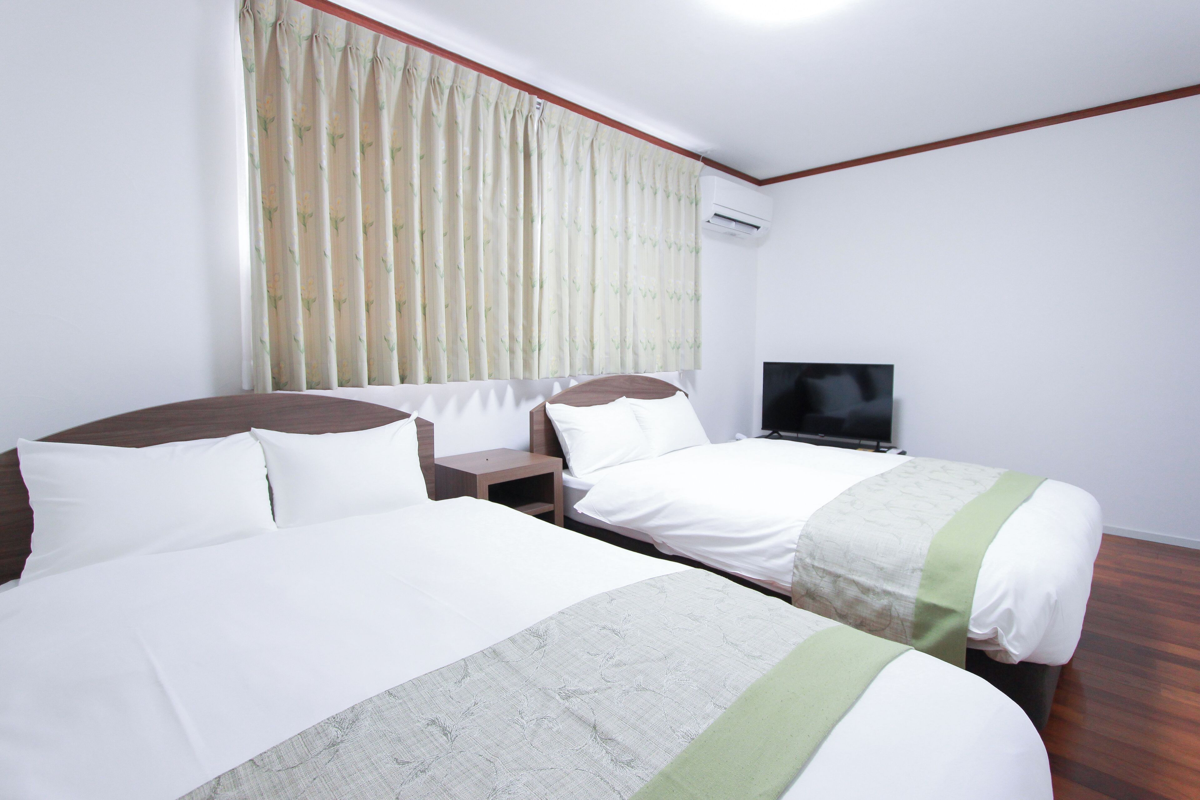 A hotel room with two beds, a TV, and an air conditioning unit.