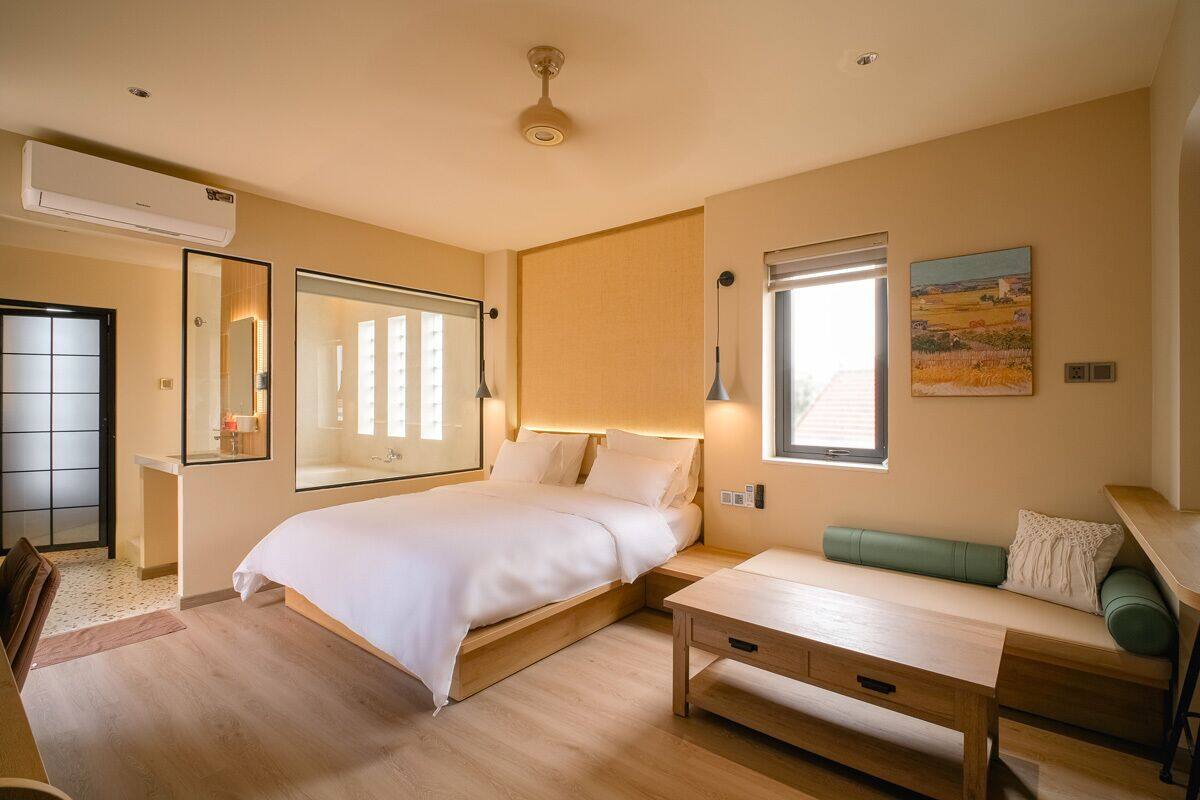 Un dormitorio moderno con cama, mesita de noche y un área de descanso con un banco.