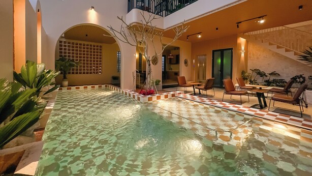 Una piscina interna con pavimento a scacchi, circondata da sedie a sdraio e una scala che conduce a un livello superiore.