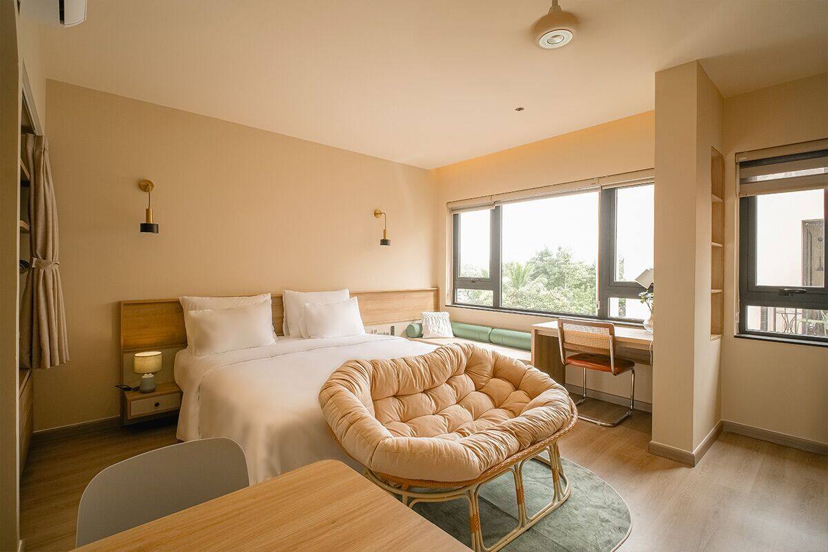Habitación de hotel moderna con cama, escritorio, silla y ventanas grandes.
