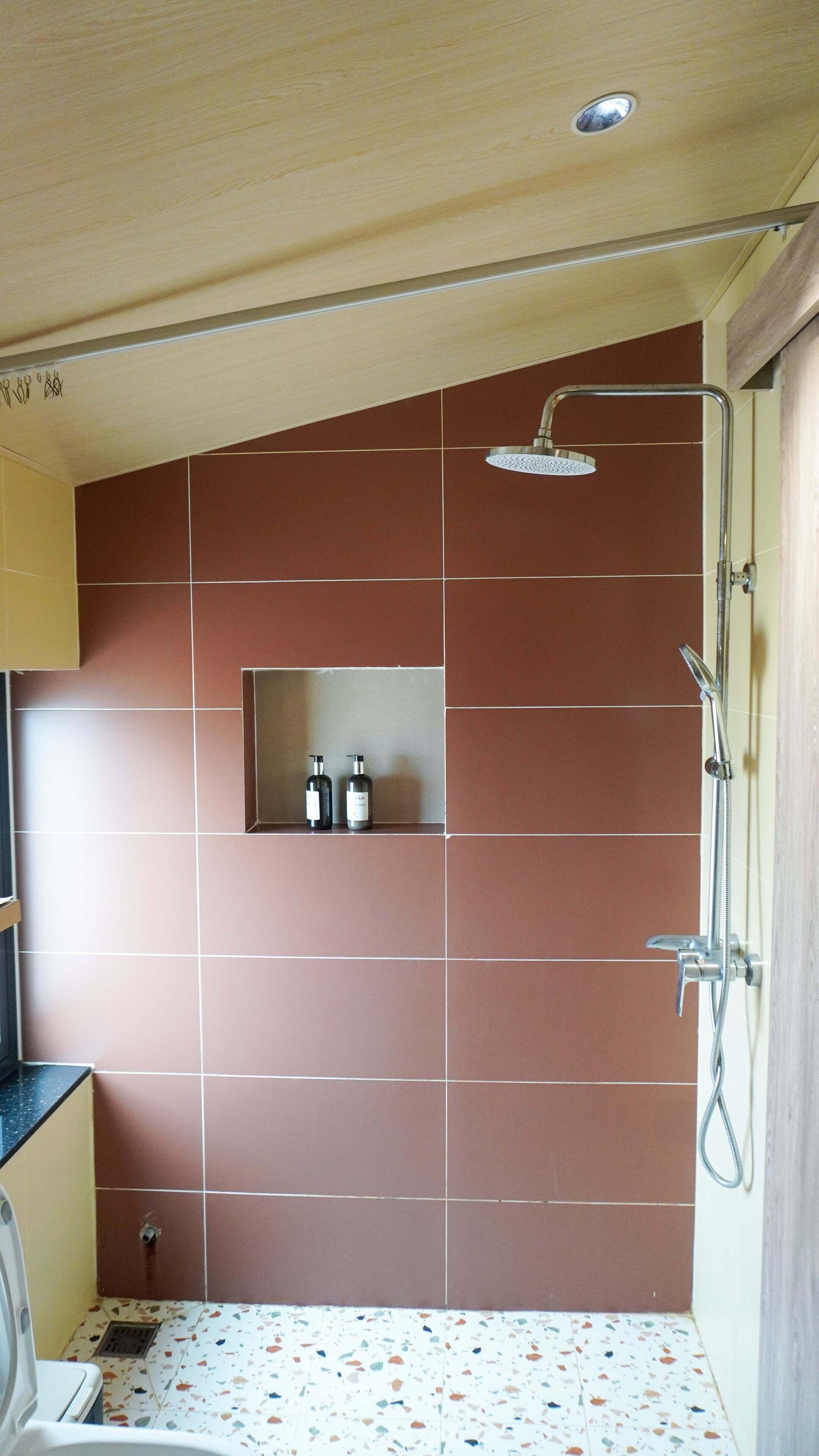A bathroom with a shower, a shelf with toiletries, and a tiled floor.