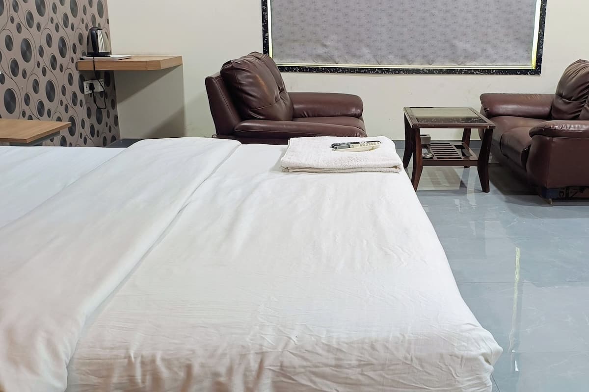 A hotel room with a large bed, two brown leather sofas, a small table, and a wall-mounted TV.