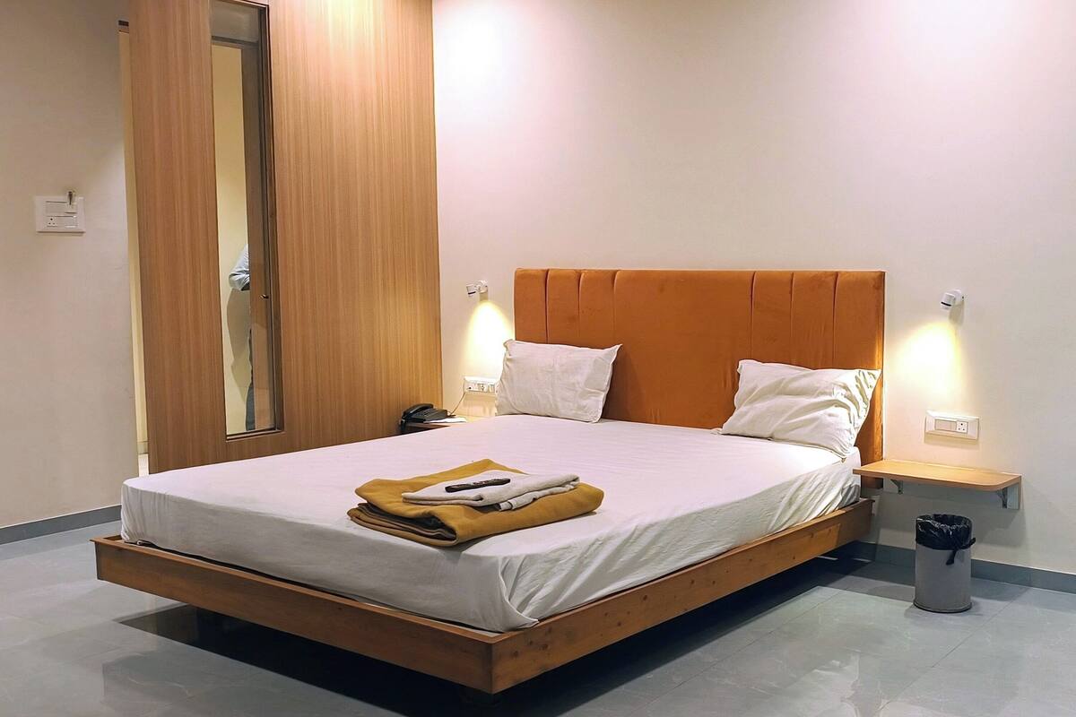 A modern bedroom with a wooden bed frame, white bedding, and a bedside table with a lamp.