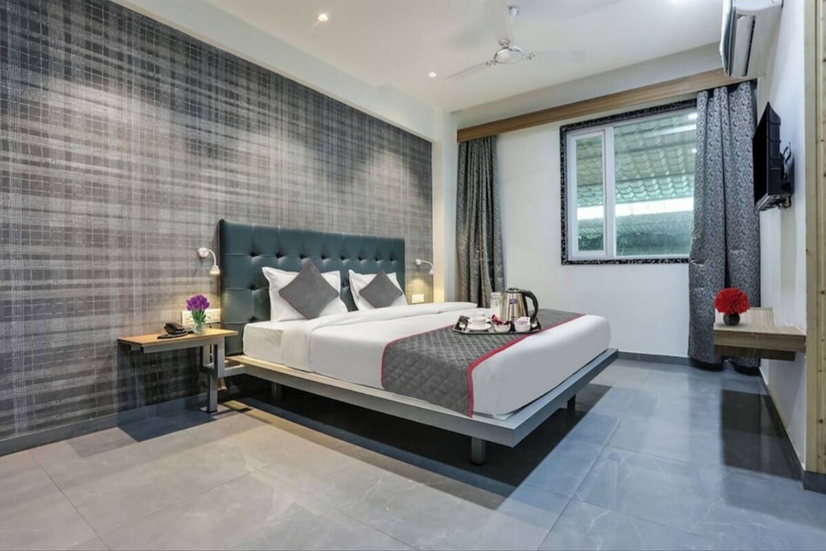 A modern hotel room with a large bed, a nightstand, a TV, and a window with curtains.