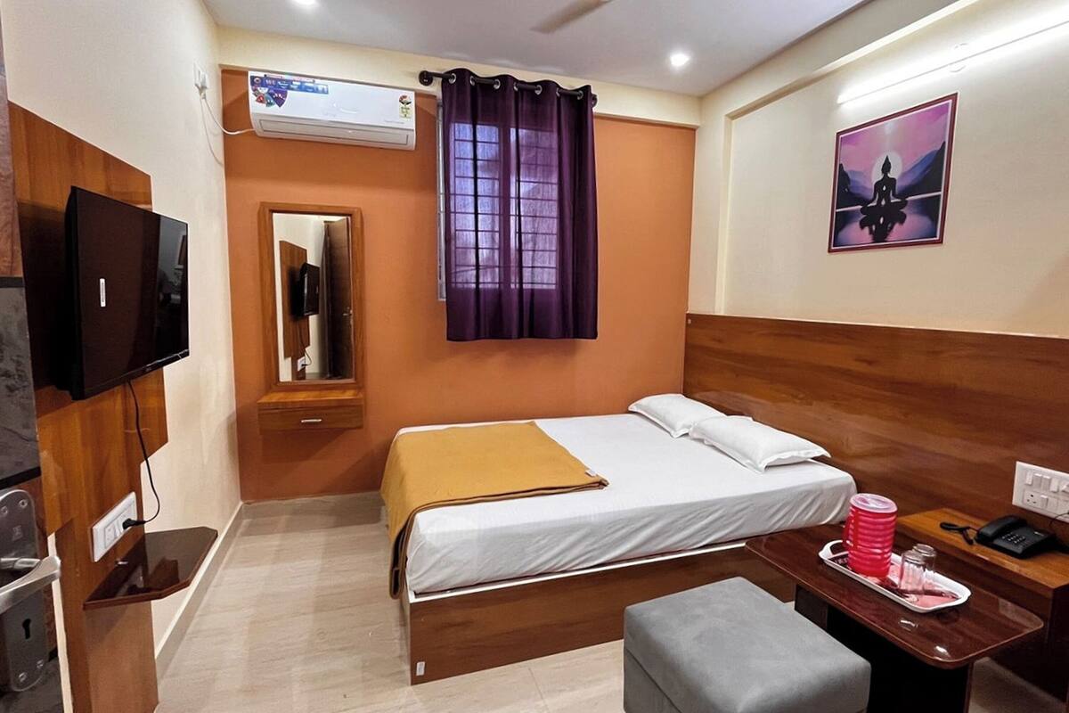 A hotel room with a bed, a TV, a desk with a phone, and a window with purple curtains.