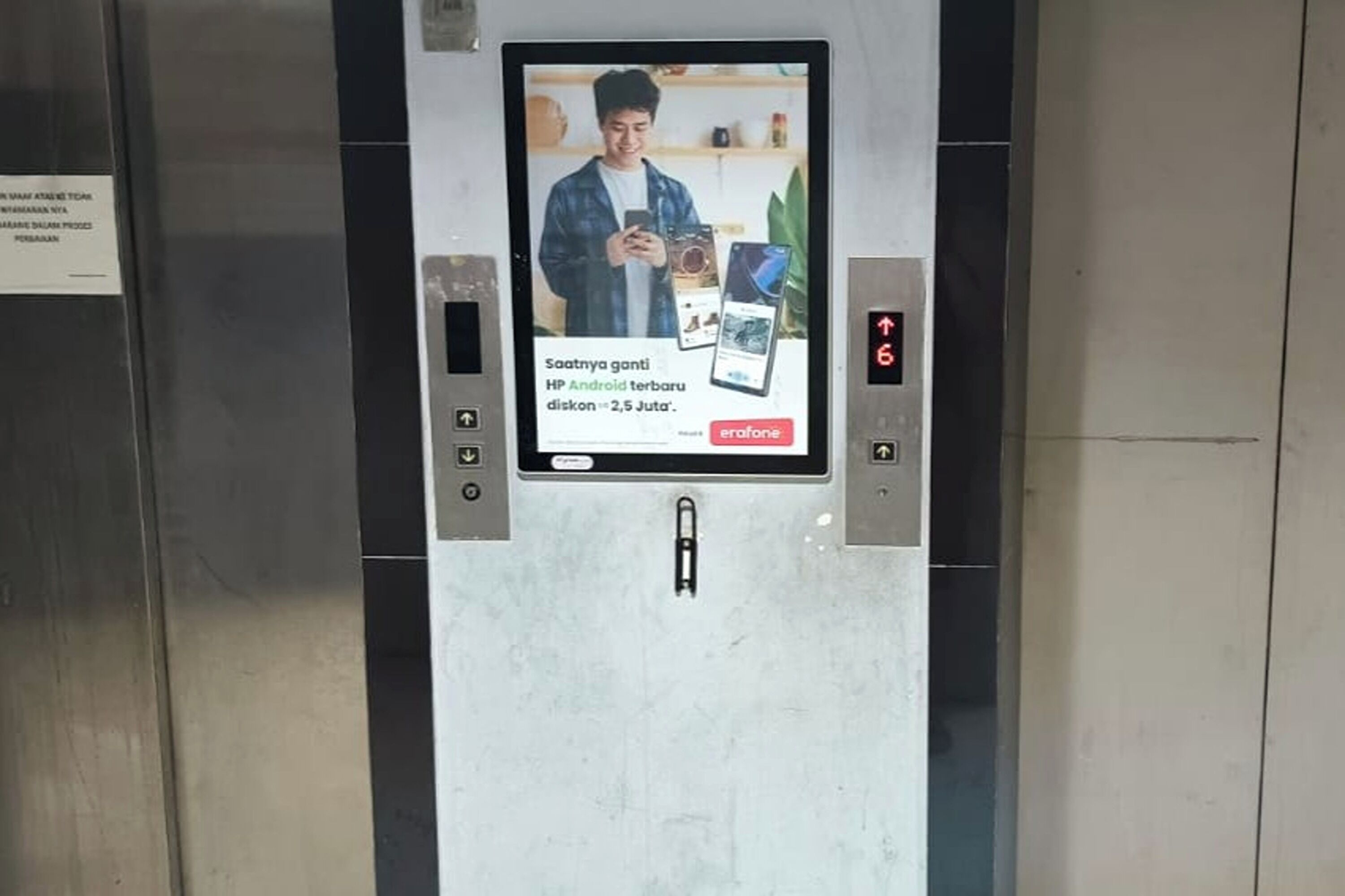 An elevator with a digital advertisement screen displaying a person using a smartphone.