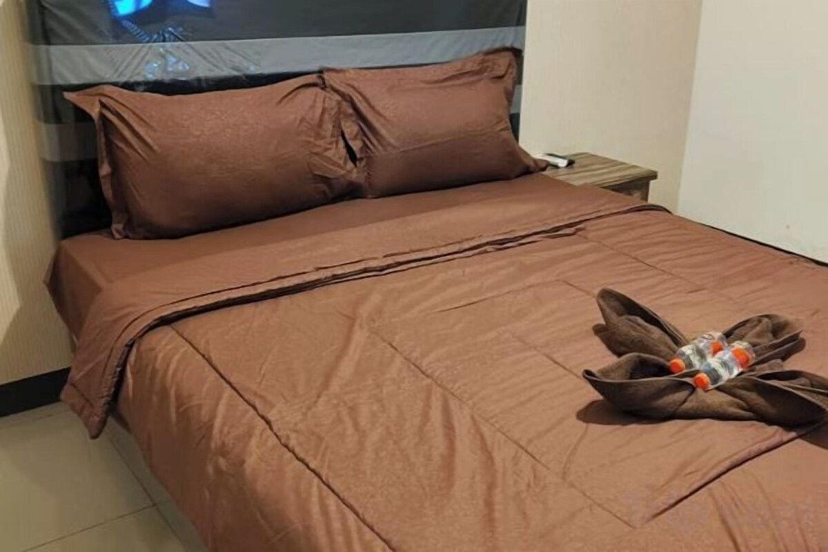 Un lit avec une couverture marron et des oreillers, une table de chevet avec une lampe et une serviette sur le lit.