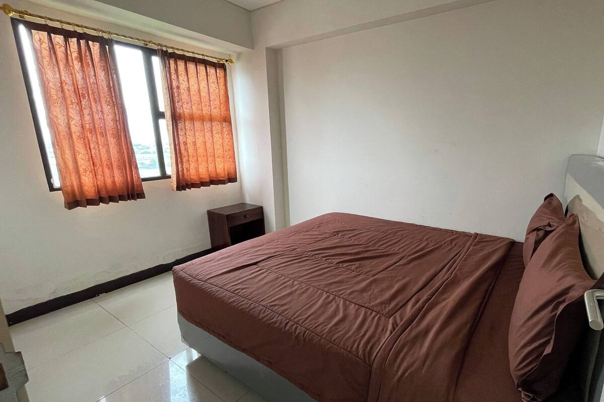 Une chambre à coucher avec un lit, des rideaux, une table de chevet et une fenêtre.