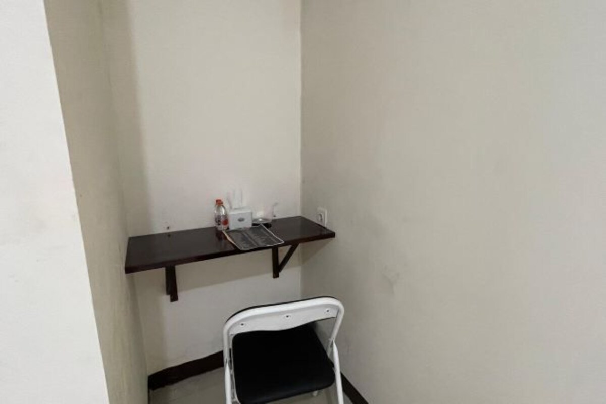 Une petite pièce avec une chaise blanche, un bureau en bois foncé et une étagère blanche sur laquelle sont posés quelques objets.