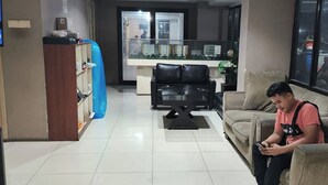 A living room with a sofa, a coffee table, and a person sitting on the sofa using a mobile device.