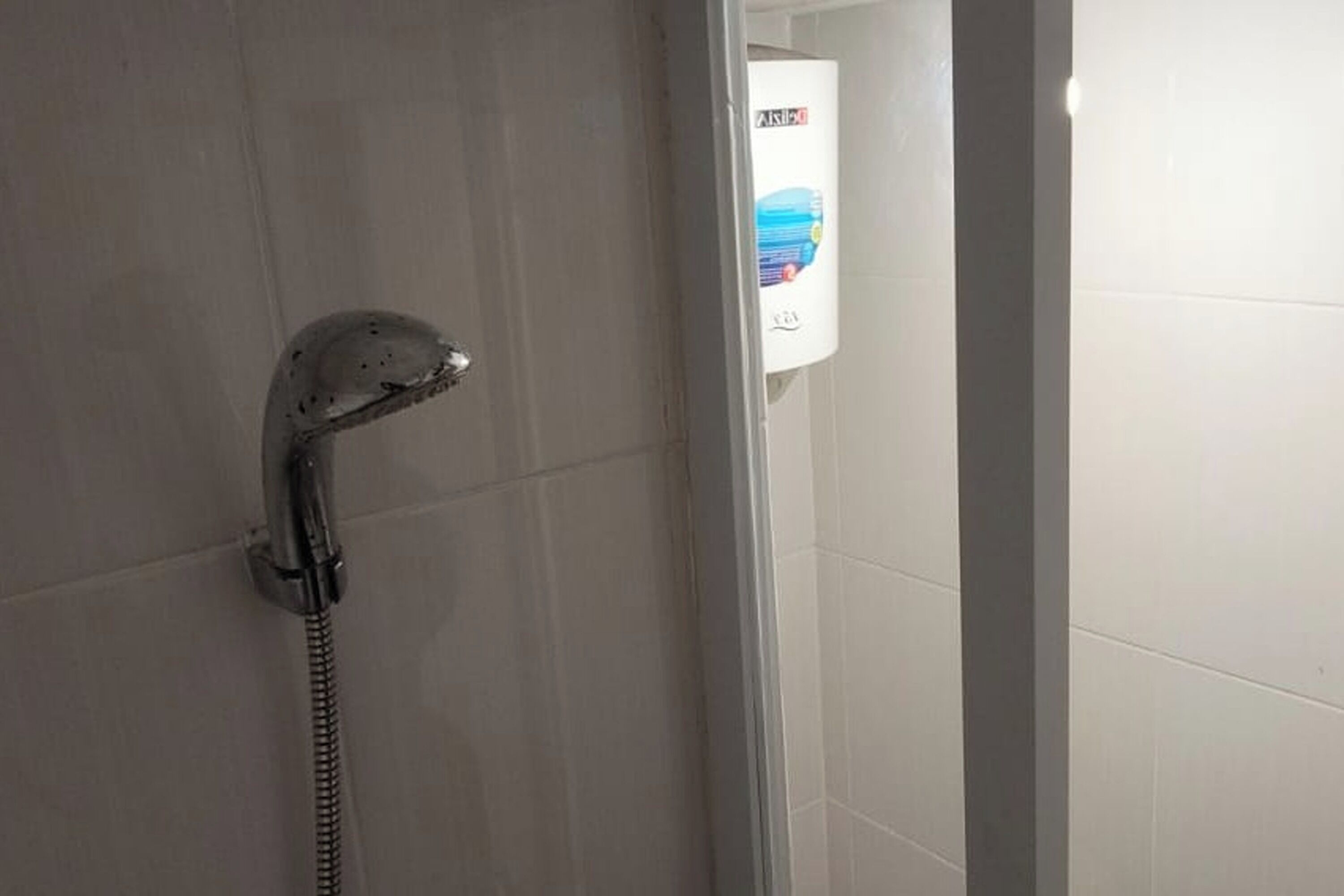 Een douche met een handdouche, boiler en betegelde wand.
