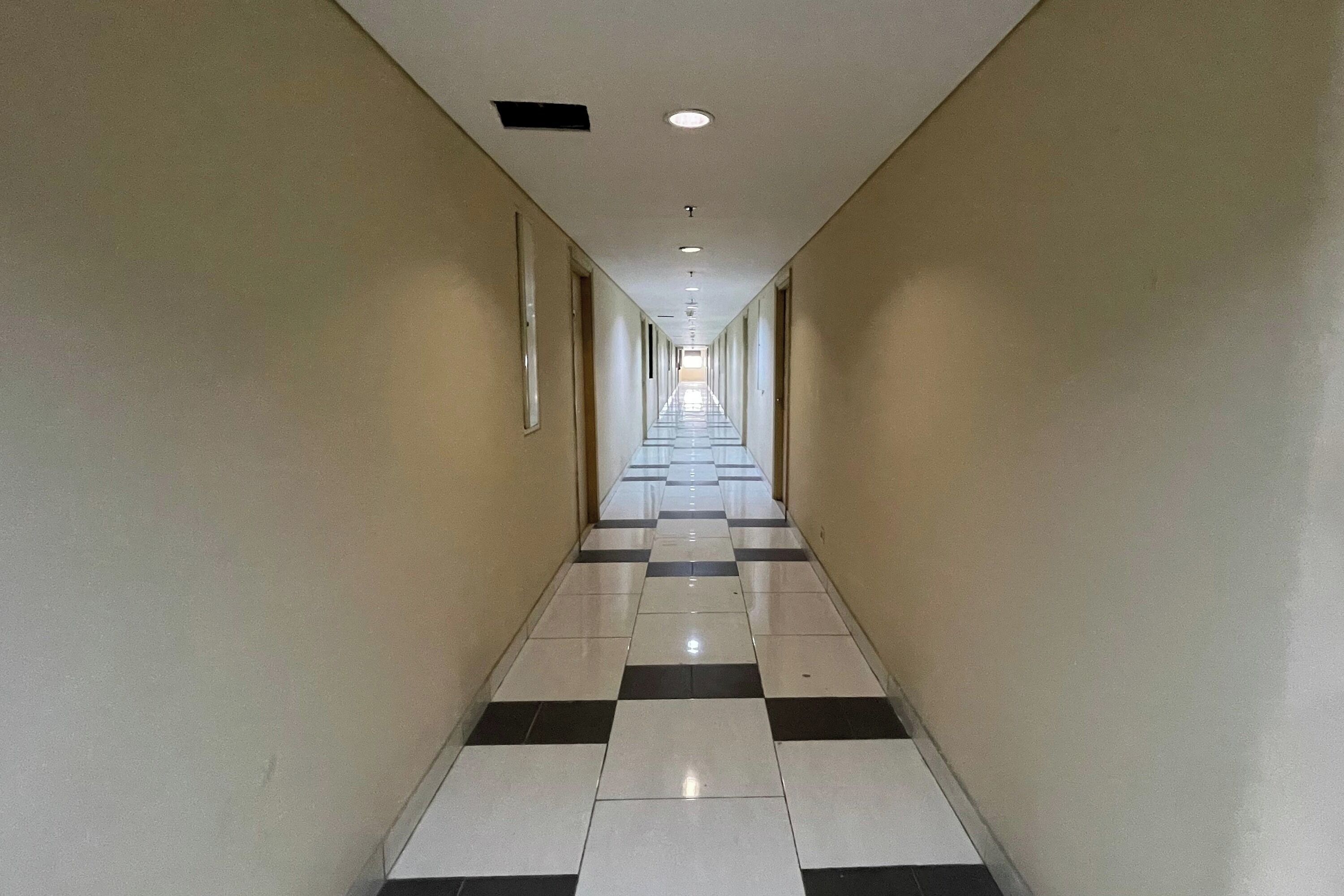 A long, narrow hallway with a checkered floor pattern and white walls.